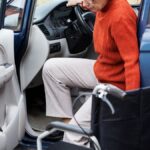 Mulher idosa com dificuldades desce do carro para usar cadeira de rodas