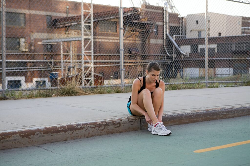 Mulher sentada na calçada, com os pés na guia, arrumando os tênis.