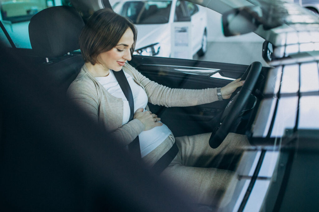 Jovem mulher grávida testando um carro no showroom