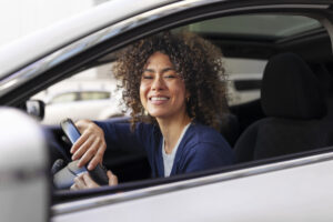 Mulher sorridente dentro de carro, olhando pela janela.