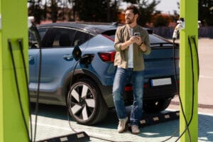 Man charging electric car and using smartphone at charging station