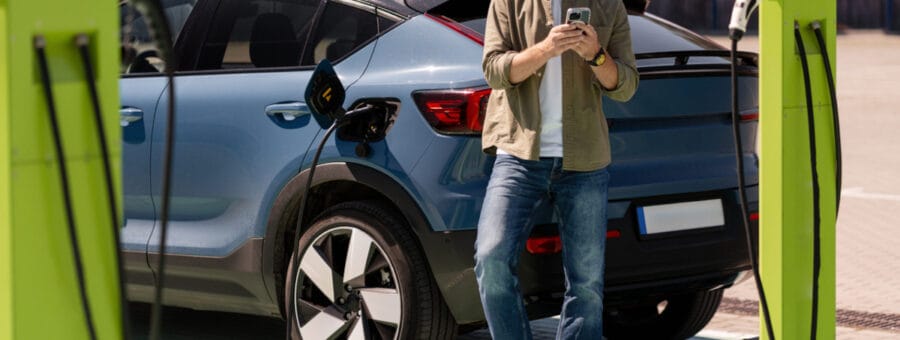 Man charging electric car and using smartphone at charging station