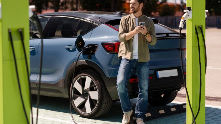 Man charging electric car and using smartphone at charging station