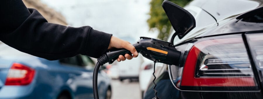 Woman near electric car. Vehicle charged at the charging station.