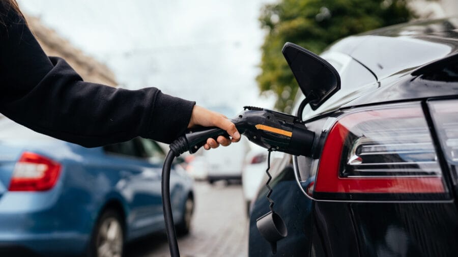 Woman near electric car. Vehicle charged at the charging station.