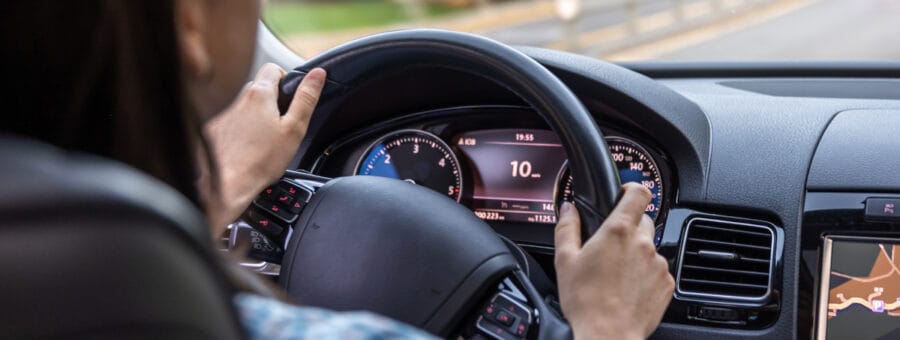 Woman driving a car, hands on the wheel close-up, view from the back to the road.