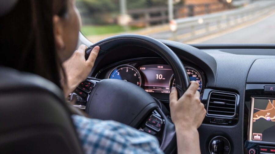 Woman driving a car, hands on the wheel close-up, view from the back to the road.